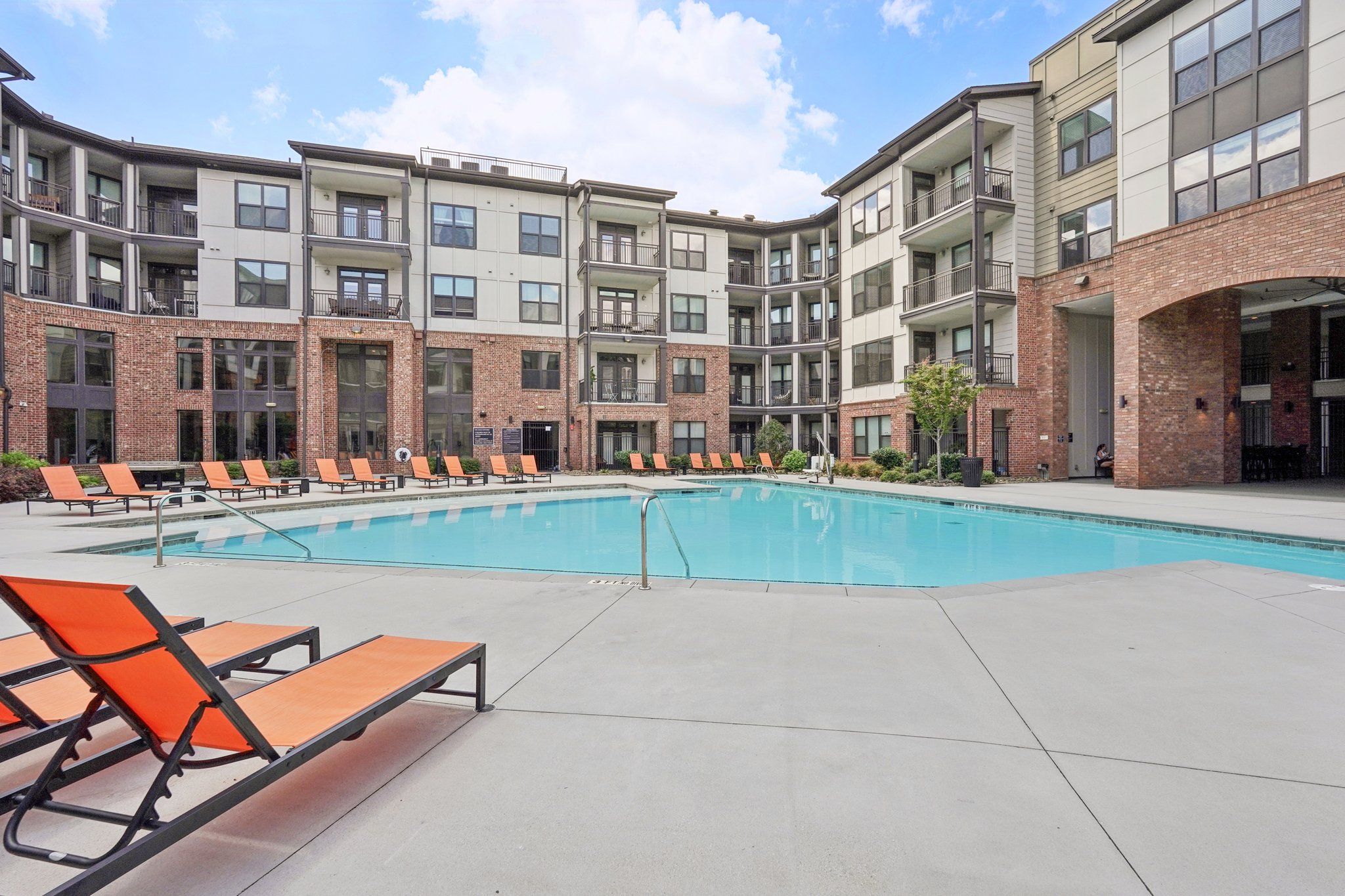 A swimming pool surrounded by orange lounge chairs and apartment buildings.